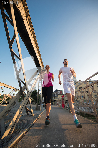 Image of young couple jogging across the bridge in the city