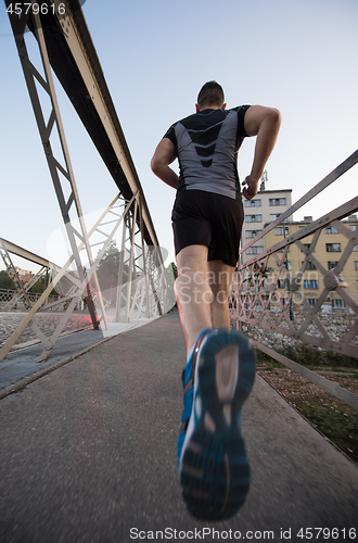 Image of man jogging across the bridge at sunny morning