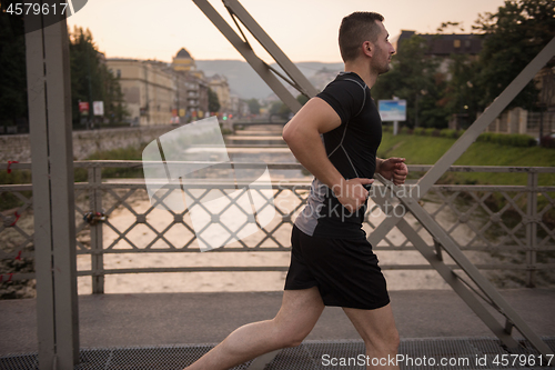 Image of man jogging across the bridge at sunny morning