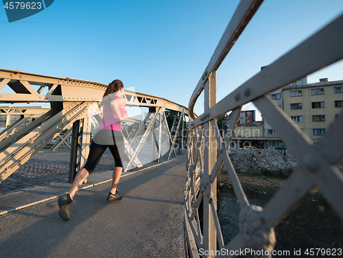 Image of woman jogging across the bridge at sunny morning