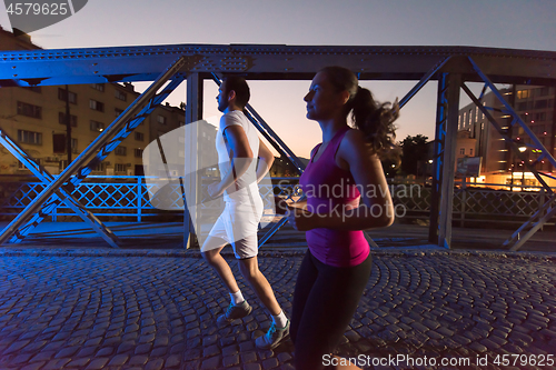 Image of couple jogging across the bridge in the city