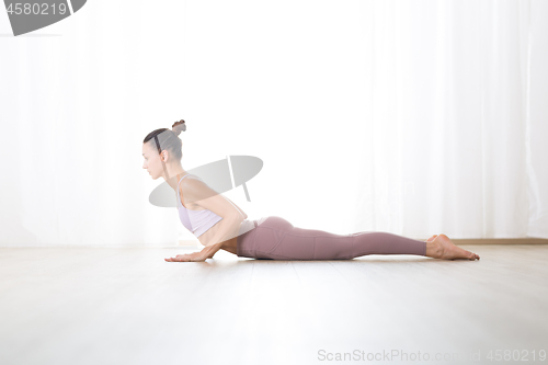 Image of Portrait of gorgeous active sporty young woman practicing yoga in studio. Beautiful girl practice Bhujangasana, cobra yoga pose. Healthy active lifestyle, working out indoors in gym