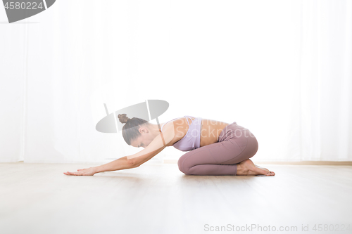 Image of Portrait of gorgeous active sporty young woman practicing yoga in studio. Beautiful girl practice Ardha Kurmasana, half tortoise yoga pose. Healthy active lifestyle, working out indoors in gym