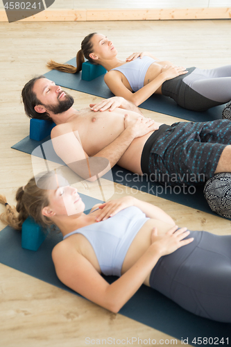 Image of Restorative yoga with a bolster. Group of young sporty attractive people in yoga studio, lying on bolster cushion, stretching and relaxing during restorative yoga. Healthy active lifestyle