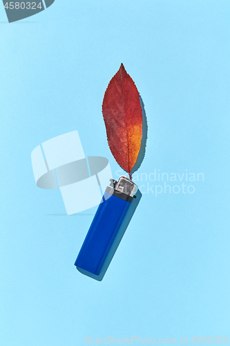 Image of Creative composition blue lighter with fire from fall red leaf and hard shadows.