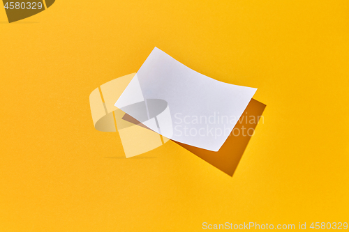 Image of Sheet of blank paper with hard shadows on an yellow.