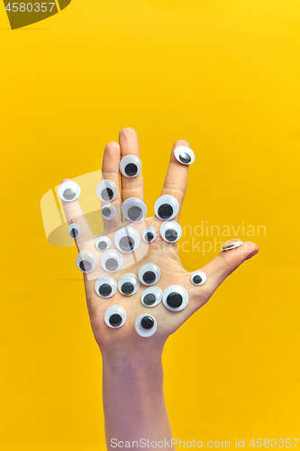 Image of Woman\'s hand with plastic eyes on an yellow background.