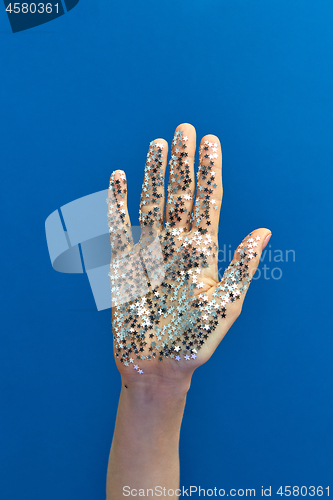 Image of Girl\'s hand with glitter silver small stars on a blue background.