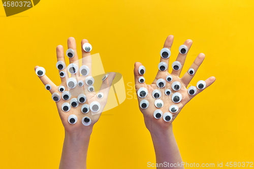 Image of Two girl\'s hands with plastic eyes on an yellow background.