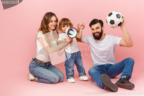 Image of happy father and son playing together with soccer ball on pink