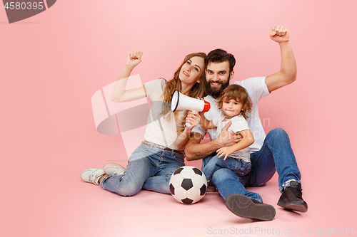 Image of happy father and son playing together with soccer ball on pink