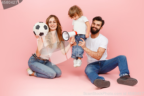 Image of happy father and son playing together with soccer ball on pink