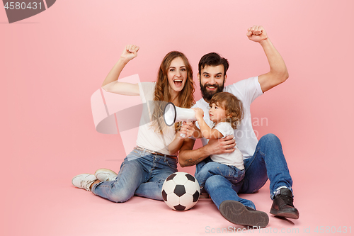 Image of happy father and son playing together with soccer ball on pink