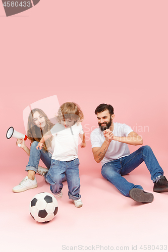 Image of happy father and son playing together with soccer ball on pink