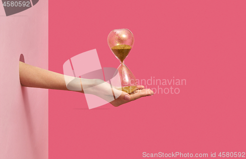 Image of Sandglass on a woman\'s hand on a duotone background.