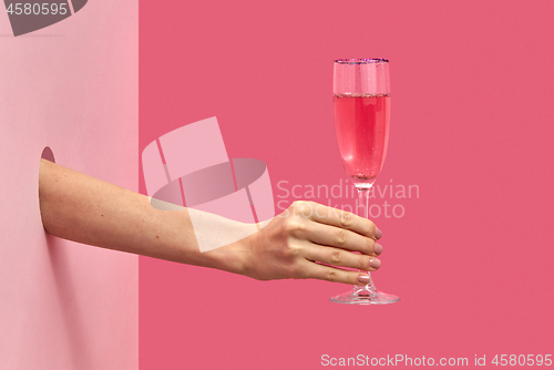 Image of Woman\'s hand holds glass of rose wine with soft shadows.