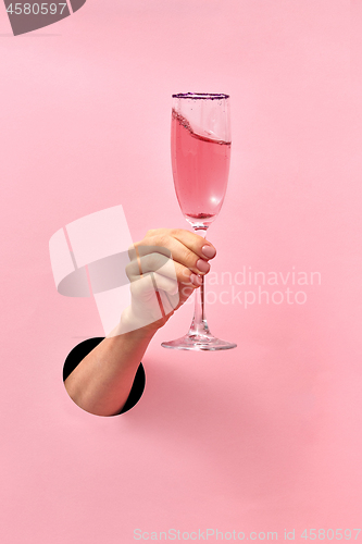 Image of Rose wine glass in a female\'s hand from the hole in the wall.