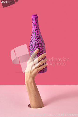 Image of Female\'s hand with painted black spots champagne bottle.