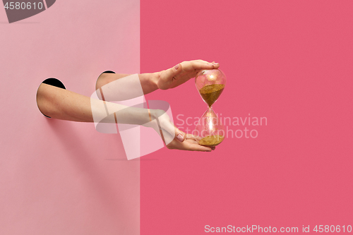 Image of Female\'s hands hold hourglass on a duotone background.