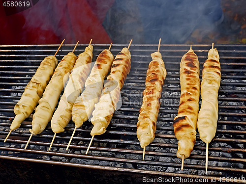 Image of Meat dish wrapped in dough around wooden sticks is grilled