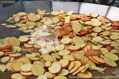 Image of A lot of sliced potato slices are fried in big steel pan