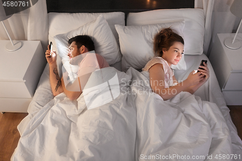 Image of couple using smartphones in bed at night