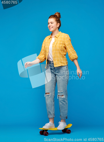 Image of red haired teenage girl riding on short skateboard