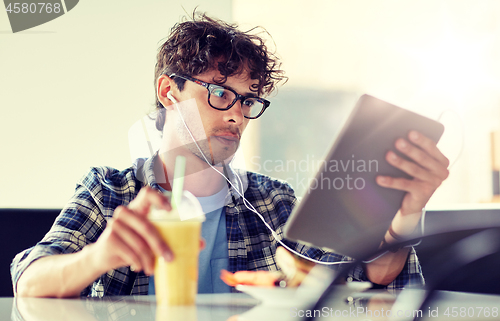 Image of man with tablet pc and earphones sitting at cafe