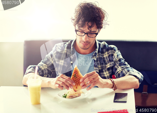 Image of happy man eating sandwich at cafe for lunch