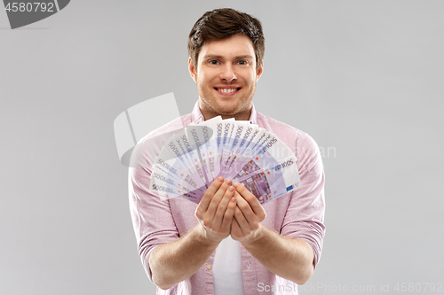 Image of smiling young man with fan of euro money over grey