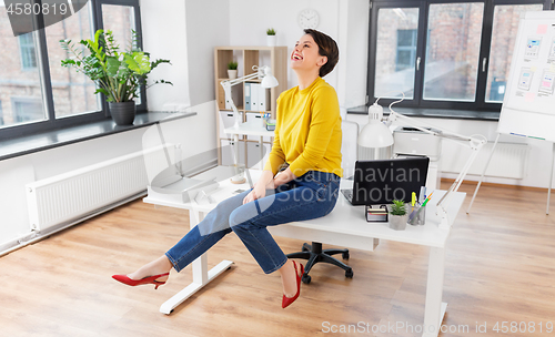 Image of happy businesswoman sitting on desk at office