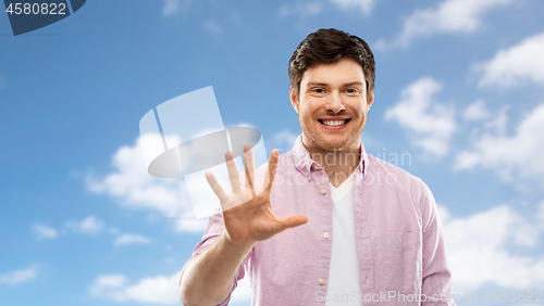 Image of young man showing five fingers over sky