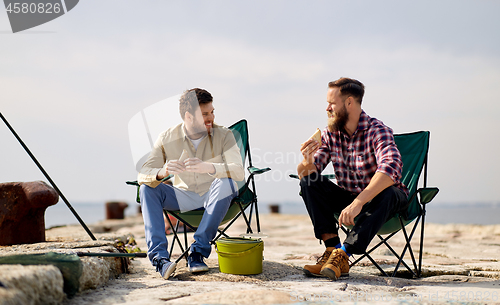 Image of happy friends fishing and eating sandwiches