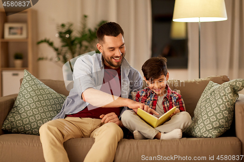 Image of happy father and son reading book sofa at home