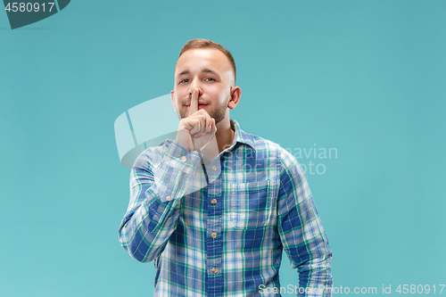 Image of The young man whispering a secret behind her hand over blue background