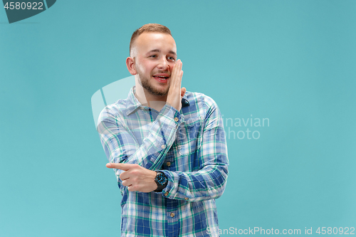 Image of The young man whispering a secret behind her hand over blue background