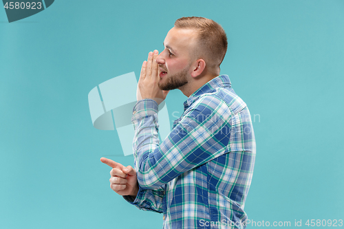 Image of The young man whispering a secret behind her hand over blue background