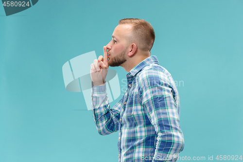 Image of The young man whispering a secret behind her hand over blue background