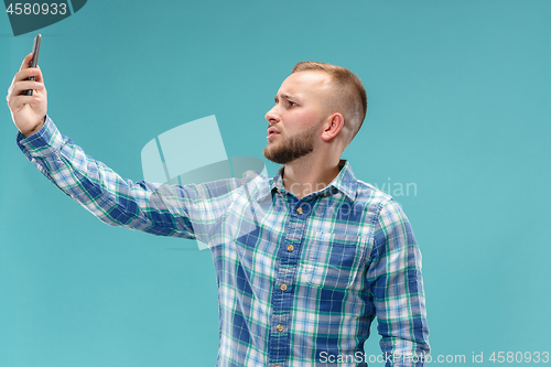 Image of Portrait of attractive young man taking a selfie with his smartphone. Isolated on blue background.