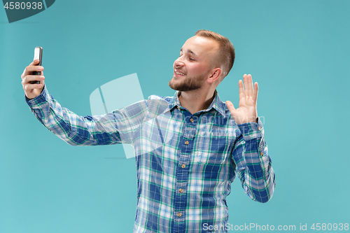 Image of Portrait of attractive young man taking a selfie with his smartphone. Isolated on blue background.