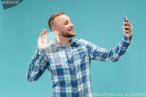 Image of Portrait of attractive young man taking a selfie with his smartphone. Isolated on blue background.