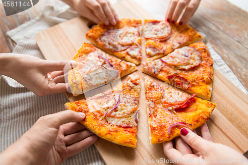 Image of close up of hands sharing pizza on wooden table