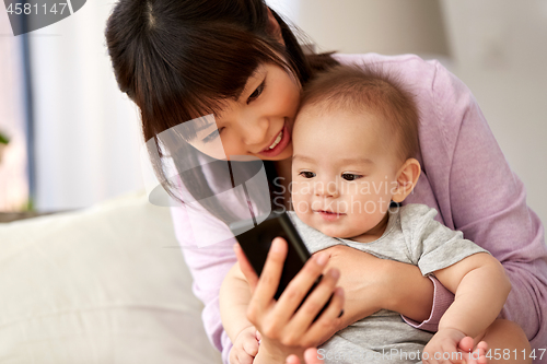 Image of asian mother with baby son taking selfie at home