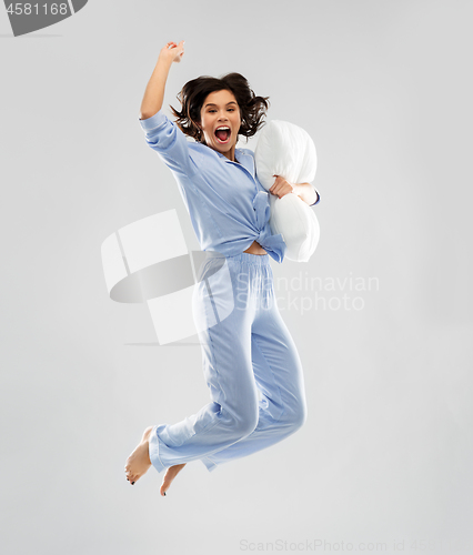 Image of happy woman in blue pajama jumping with pillow