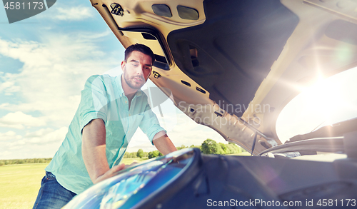 Image of man with open hood of broken car at countryside