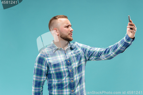 Image of Portrait of attractive young man taking a selfie with his smartphone. Isolated on blue background.