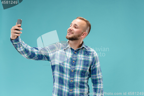 Image of Portrait of attractive young man taking a selfie with his smartphone. Isolated on blue background.