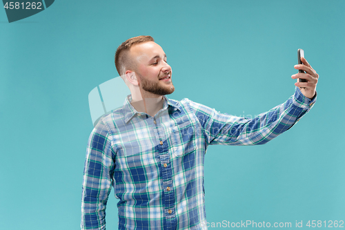 Image of Portrait of attractive young man taking a selfie with his smartphone. Isolated on blue background.