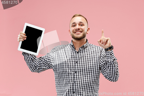 Image of Studio picture of positive man isolated on pink background standing in casual clothes holding tablet and showing it blank screen with happy smile