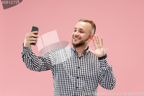 Image of Portrait of attractive young man taking a selfie with his smartphone. Isolated on pink background.